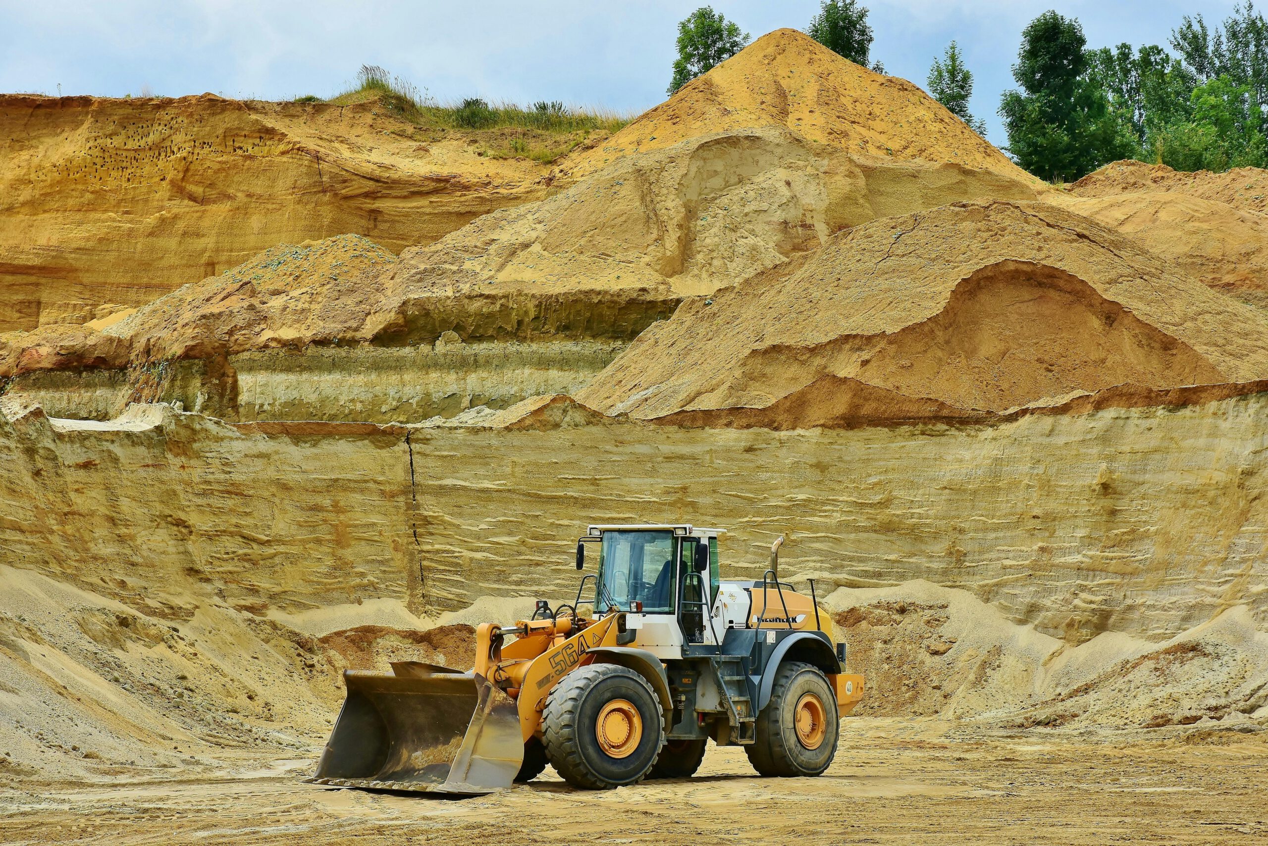 An excavator working in an open pit mine surrounded by sandy terrain and clear sky.
